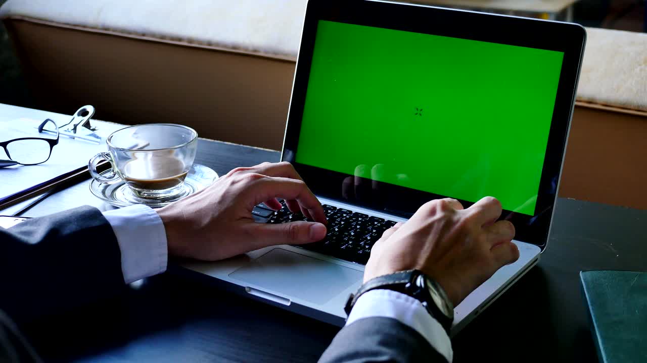 Nærbillede af forretningsmand, der bruger en bærbar computer med grøn skærm på skrivebordet.