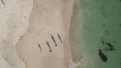 People-walk-along-the-shoreline-while-casting-their-shadows-in-front-of-them