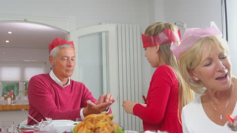 grandparents with grandchildren playing with christmas cracker gifts whilst eating meal together