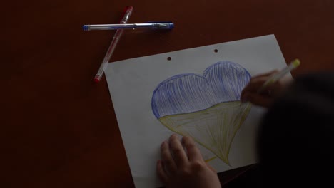 children's hands of a child draw a heart-shaped icon with the image of the national flag of ukraine. view from above. children against war. children's drawing for peace in ukraine