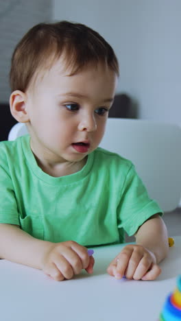 Active healthy Caucasian baby playing at home sitting at the desk. Kid holds the toys and screams. Vertical video
