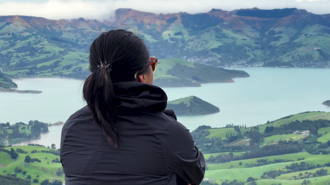 Woman gazing at stunning view of Akaroa Peninsula, New Zealand's beauty, rear view