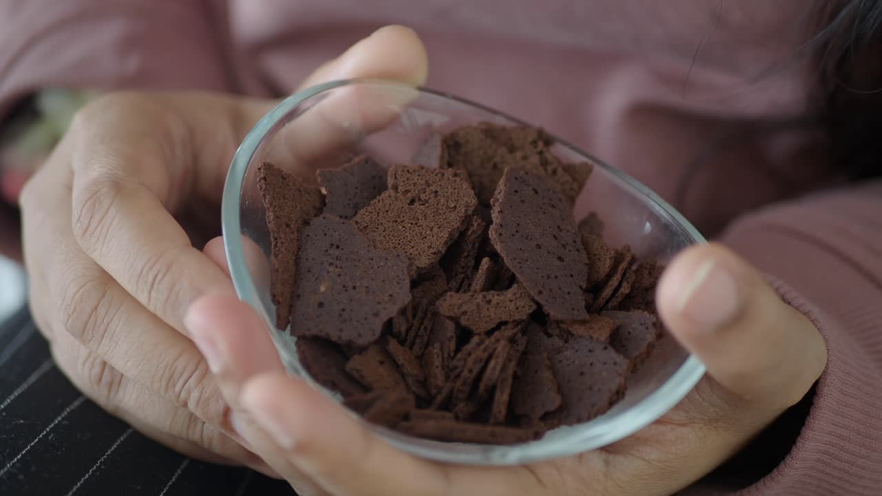 Donna che mangia biscotti al cioccolato da una ciotola di vetro