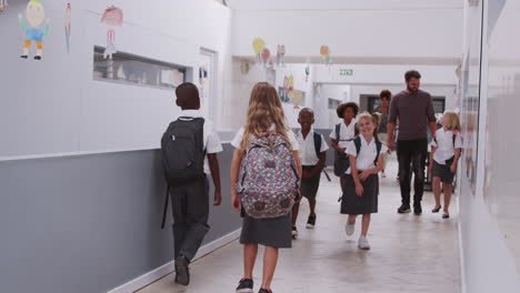 teacher and pupils walking along corridor in busy elementary school corridor