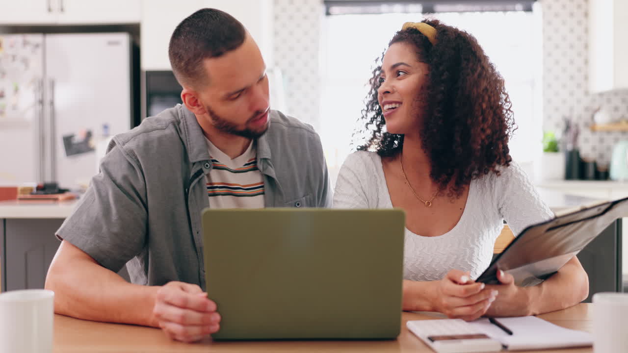 una pareja revisando documentos en una computadora portátil en una cocina.