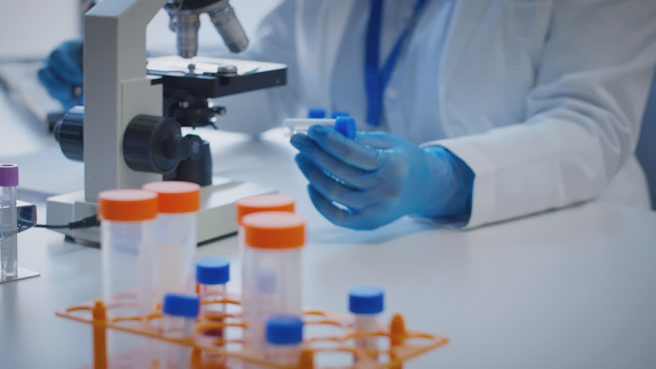 primer plano de un trabajador de laboratorio que realiza investigaciones utilizando un microscopio que sostiene un tubo de ensayo etiquetado omicron