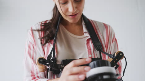 Female-Crew-Member-On-Video-Film-Set-Operating-Wireless-Follow-Focus-Module-In-White-Studio