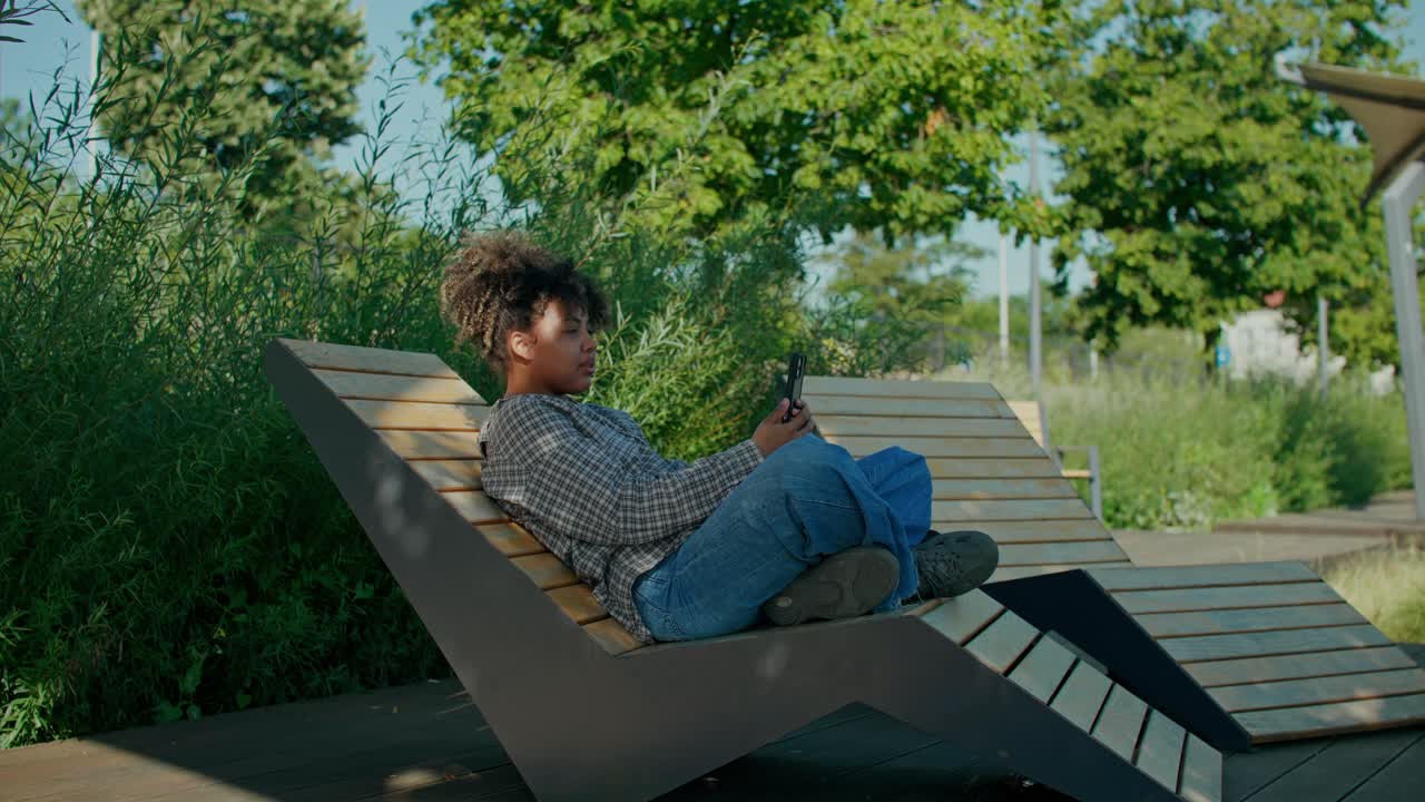 Une femme se détend sur un banc avec son téléphone dans le parc