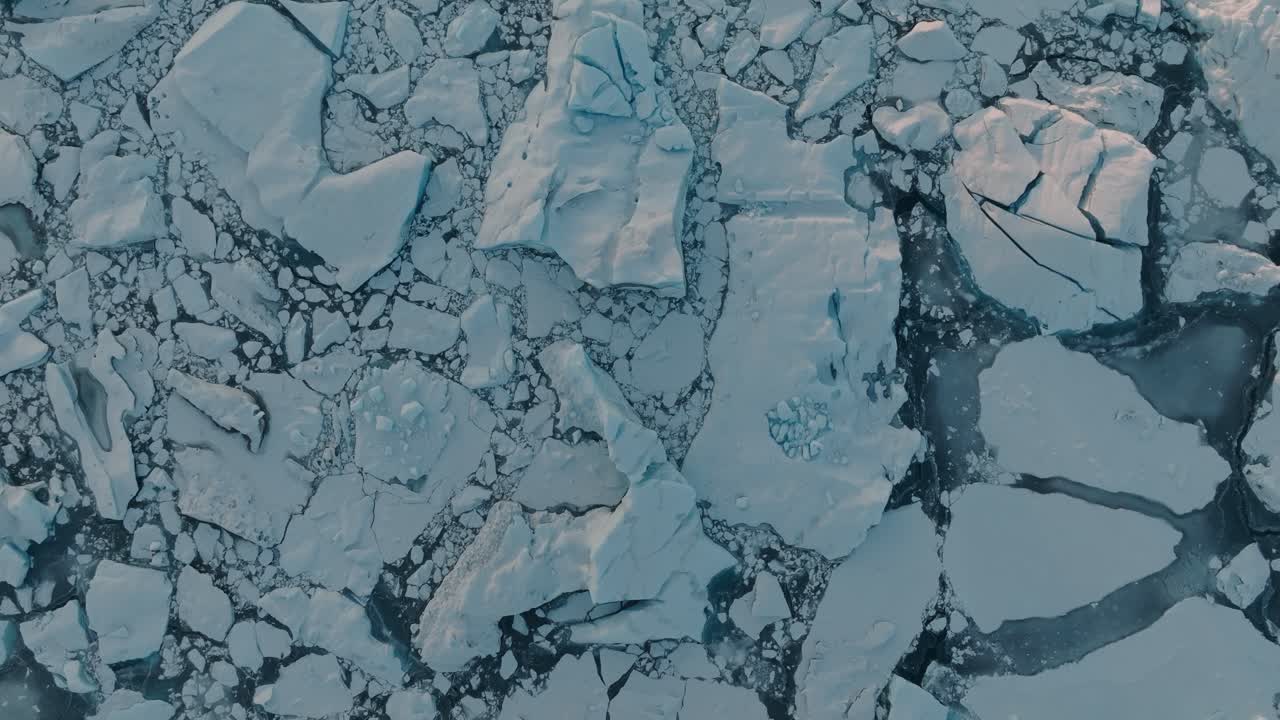 Splendide riprese drone catturano ghiaccio marino fratturato che galleggia in scure acque artiche al largo della costa islandese. Grandi blocchi di ghiaccio creano motivi drammatici separati da canali d'acqua aperti durante la stagione invernale