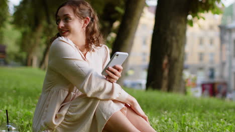 smiling young woman using smartphone typing text answering messages chatting online in city park