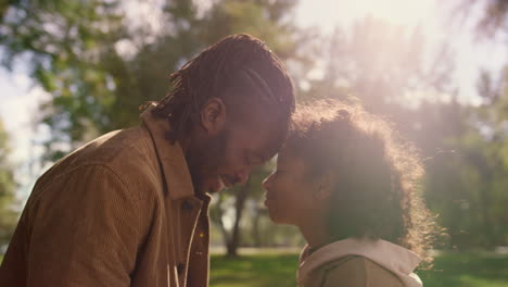 Cute-child-touching-forehead-smiling-father-in-golden-sunlight-park-portrait.