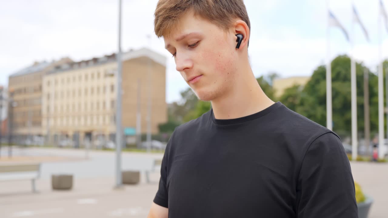 Young man in sports outfit takes out wireless earbuds to begin workout outdoors, calm moment