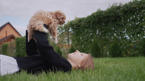 girl playing with a puppy, lying on the lawn in the backyard of the house