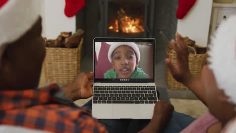 Pareja-Afroamericana-Con-Gorros-De-Papá-Noel-Usando-Una-Computadora-Portátil-Para-Una-Videollamada-Navideña-Con-Un-Niño-En-La-Pantalla