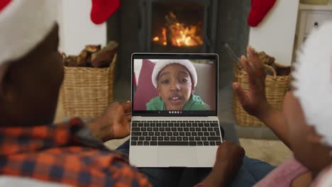 pareja afroamericana con sombreros de santa usando una computadora portátil para una videollamada de navidad con un niño en la pantalla