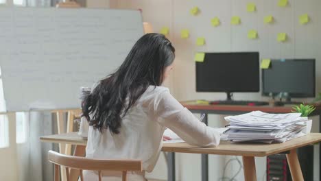 사무실 에서 문서 를 처리 하는 동안 종이 에 뭔가 쓰고 있는 아시아인 여자 의 뒷면