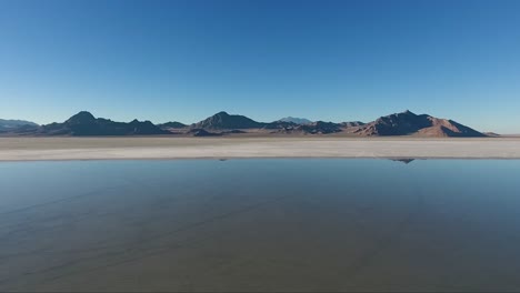 an aerial drone shot reveals smooth water covering the white salt of the bonneville salt flats and distant mountains