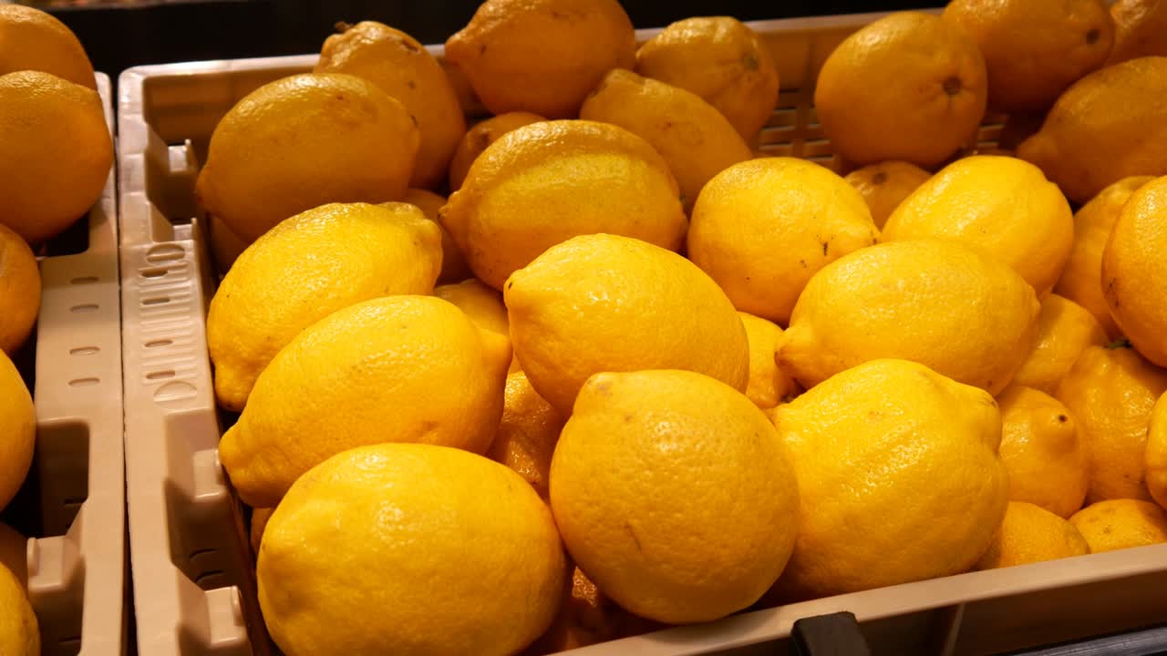 Close-up of many ripe lemons in a trading basket and a male hand takes one