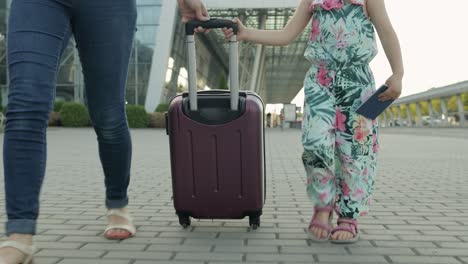 mother and daughter walking from airport. woman carrying suitcase bag. child and mom after vacation