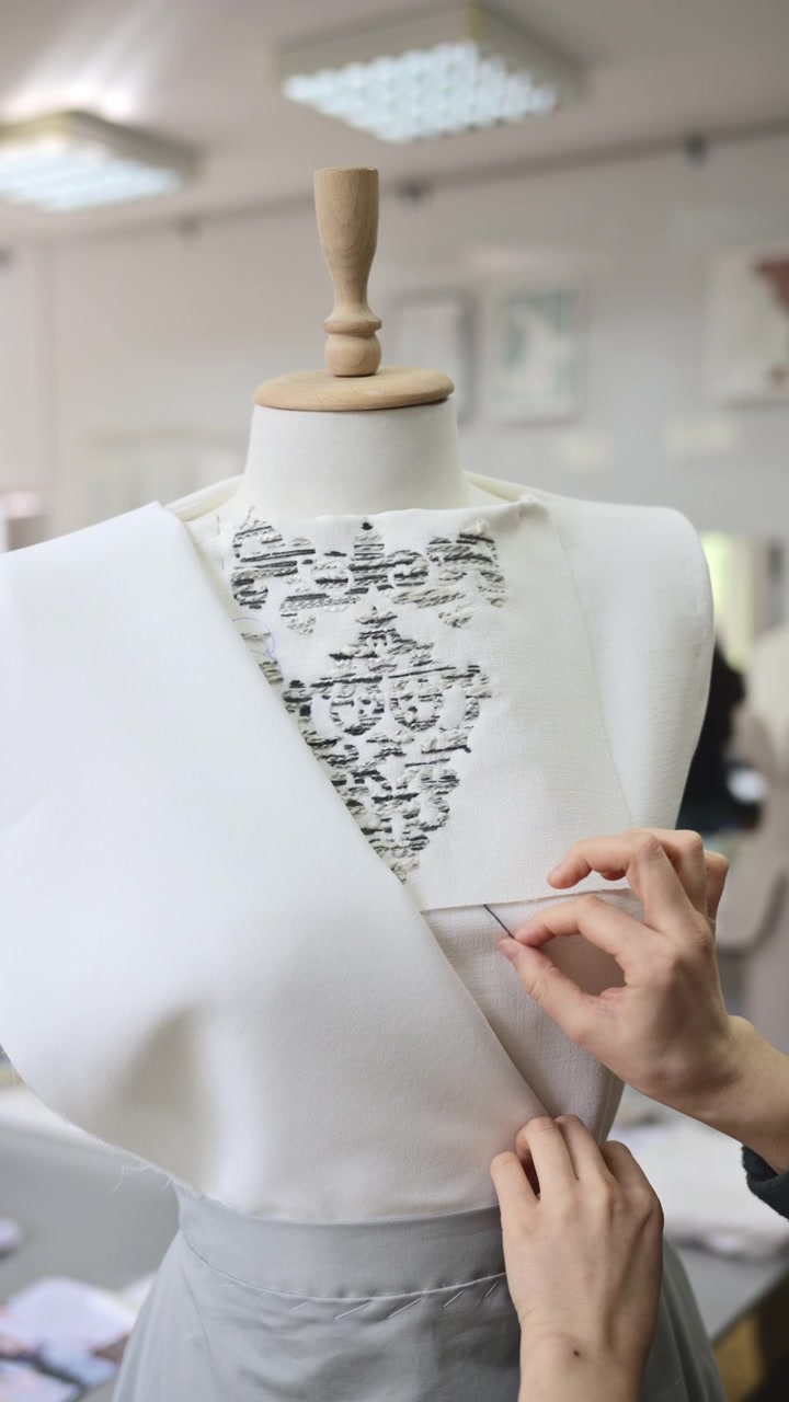 Hands carefully adjusting fabric on a dress form, securing material placement during the fitting process. Vertical