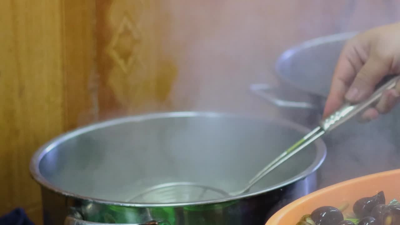 A person uses a wire mesh strainer to transfer cooked shellfish from boiling water