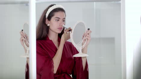 model carefully using make-up accessory and mirror as part of her routine