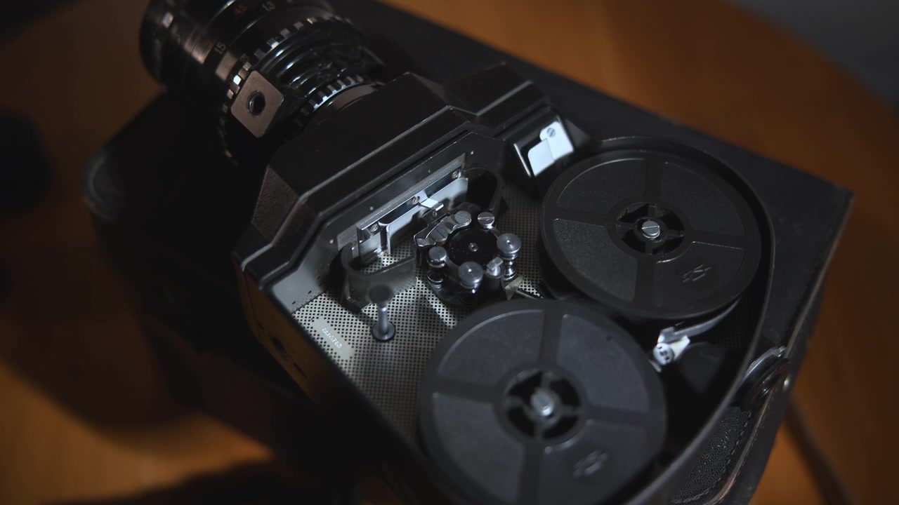 Close-up view of a hand examining an open vintage tape recorder mechanism with visible reels, metal parts, and circular components on a wooden surface under