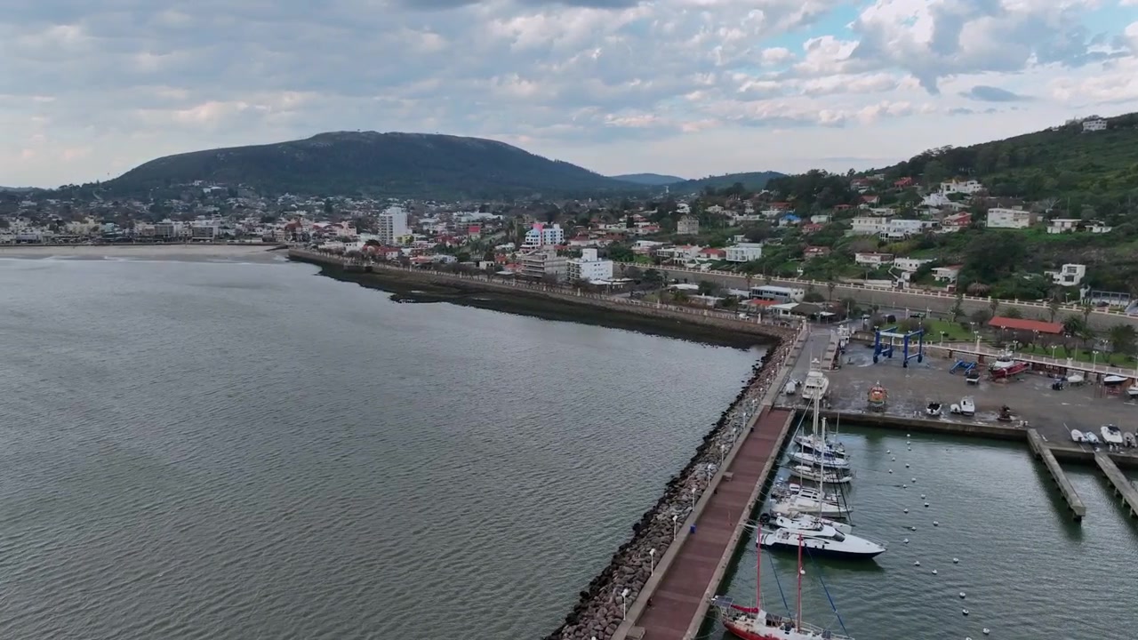Piriápolis along the Rambla de los Argentinos waterfront promenade in Piriápolis, with the pier, anchored boats, and coastal hillside cityscape expanding into view and forward push.