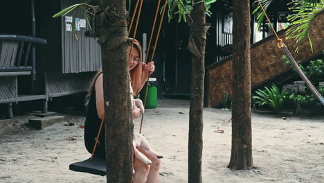 Chica-Asiática-Y-Bulldog-Francés-Relajándose-En-El-Columpio-En-El-Patio-De-La-Casa,-Zambales,-Filipinas