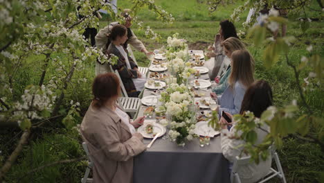 people are resting and having lunch in blooming garden in spring day sitting under blooming trees