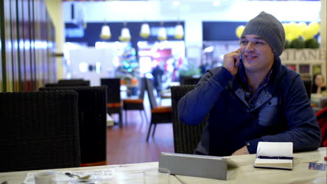 young man in cafe speaks on the phone and writes down something