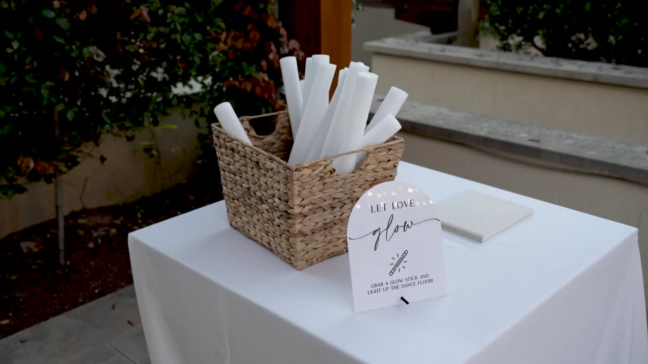 En un evento al aire libre, los invitados se reúnen alrededor de una cesta llena de pergaminos. Pueden escribir mensajes de cariño y apoyo para la pareja.