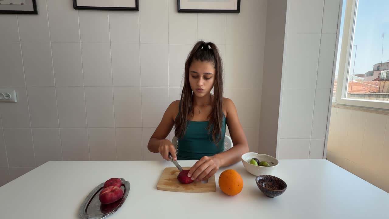 Mujer joven comiendo fruta fresca y preparando una nectarina en la cocina.