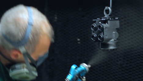 painter spraying black color on machine parts at industrial plant