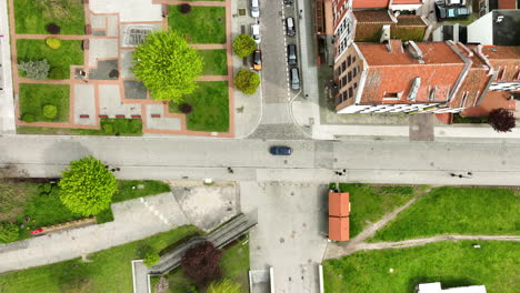 top-down aerial view of a picturesque urban setting, with vibrant green trees standing out amid red-roofed buildings, a neat urban park, and crisscrossing streets an organized, tranquil town life