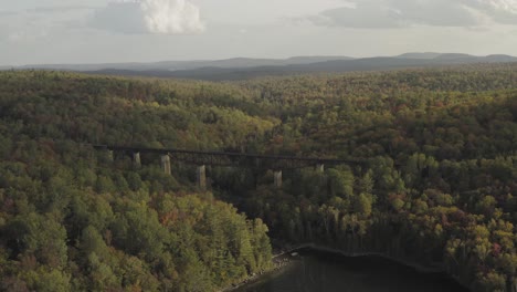 Railroad-Trestle-crossing-the-outlet-of-a-lake-with-early-fall-foliage-at-sunset-AERIAL-PULL-BACK