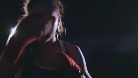 a beautiful female boxer strikes directly into the camera looking into the camera and moving forward on a dark background with a backlight. steadicam shot