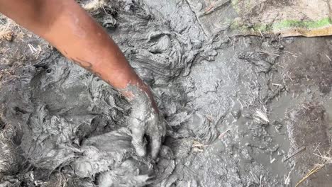 boy mixing mud to use for idol making during durga puja in bengal, india