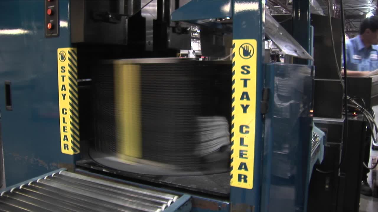 공장에서 기계가 신문을 쌓고 묶은 다음 종이 더미를 확대합니다.