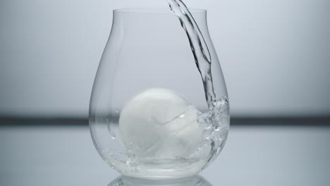 Agua-En-Cascada-Sobre-Un-Cubo-De-Hielo-Redondo-En-Un-Vaso