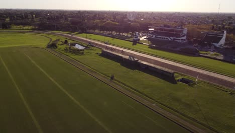 Aerial-tracking-shot-of-horses-running-on-racetrack-during-horse-race-at-sunset---San-Isidr,Argentina