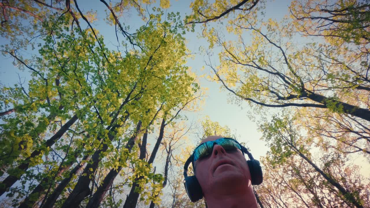 Plano contrapicado de un hombre maduro activo de unos 50 años mirando hacia la exuberante copa verde del bosque. Concepto de senderismo consciente, conexión con la naturaleza y alivio para la salud mental. Calidad 4k.