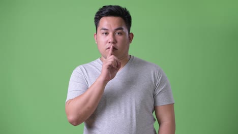 young handsome overweight asian man against green background