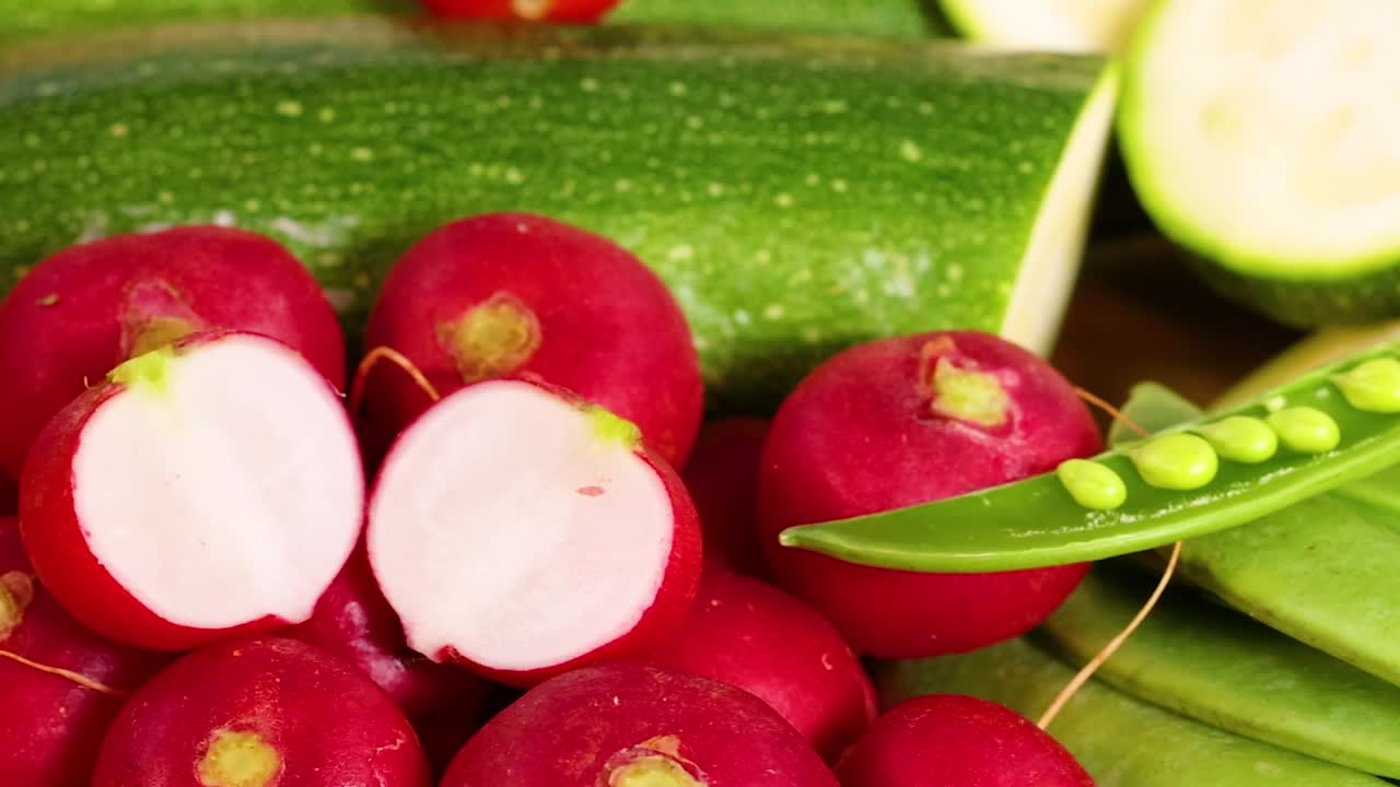 A colorful assortment of fresh vegetables including radishes, zucchini, carrots, squash, and more on a white background.