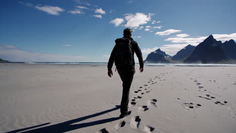 person with backpack walking on a vast sandy beach with mountains and sea