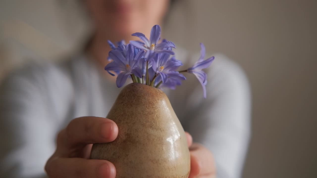 manos femeninas sosteniendo un pequeño jarrón con pequeñas flores de primavera