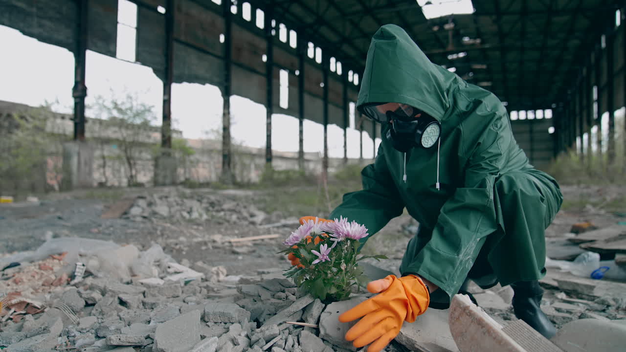 Giving new life to our planet. Ecologist in safety suit and gas mask preparing to placing flowers in abandoned place around the building trash. Biochemical attack concept