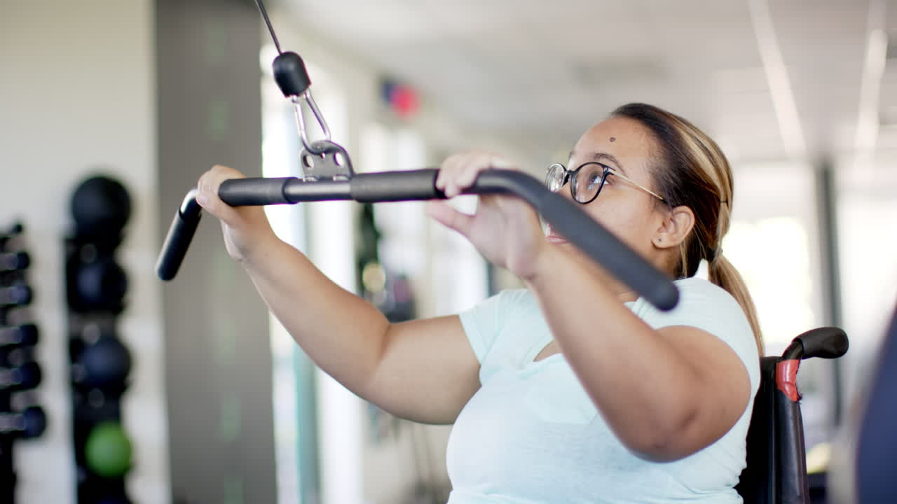 woman in wheelchair with paraplegia exercising with cable machine in rehabilitation gym