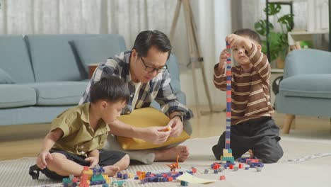 full body of asian father and sons assemble the construction set colorful plastic toy brick on a mat at home