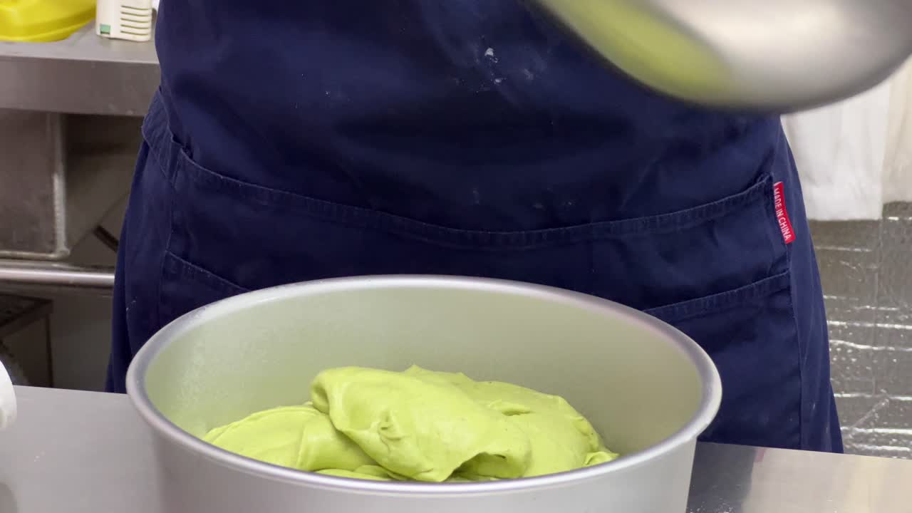 Scarping off matcha cake mixture using spatula from the mixing bowl into baking mould, delicious soft and tasty cake making in progress, close up shot